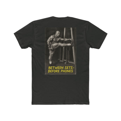 Black t-shirt with graphic of a muscular man and text 'Between Sets Before Phones' on a white background